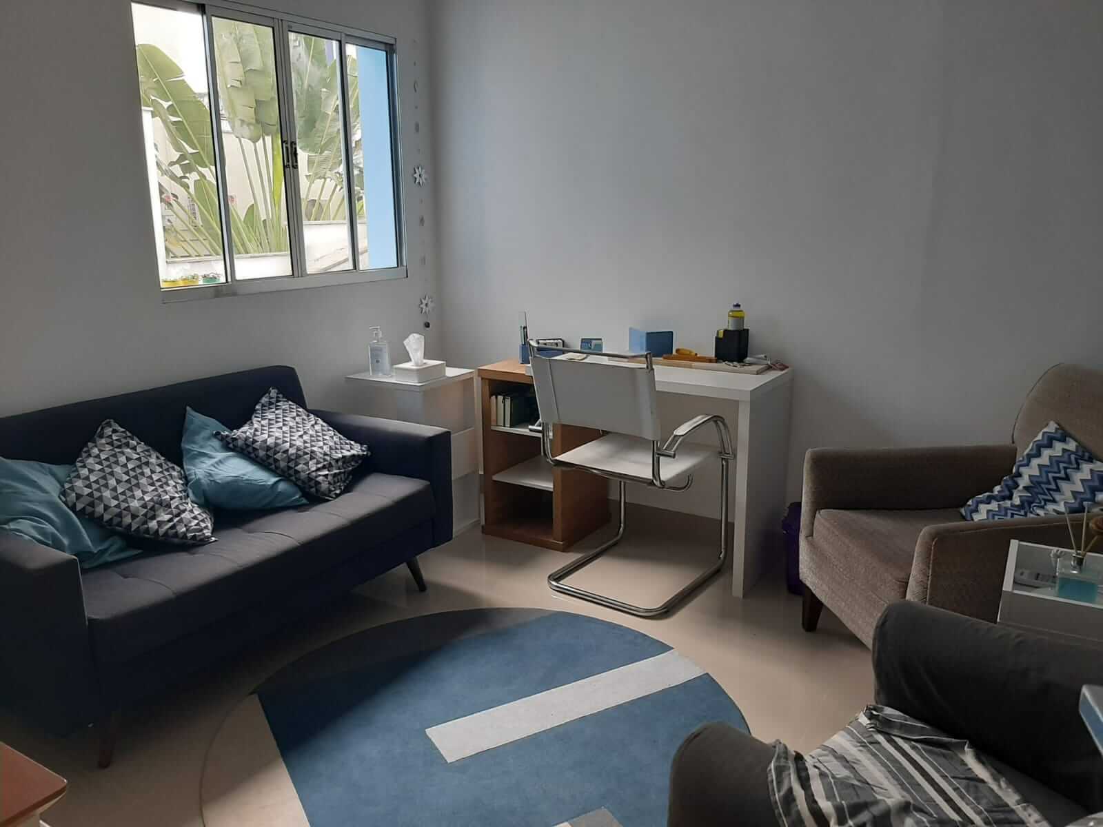 Sala de atendimento com sofá, poltronas e mesa de trabalho