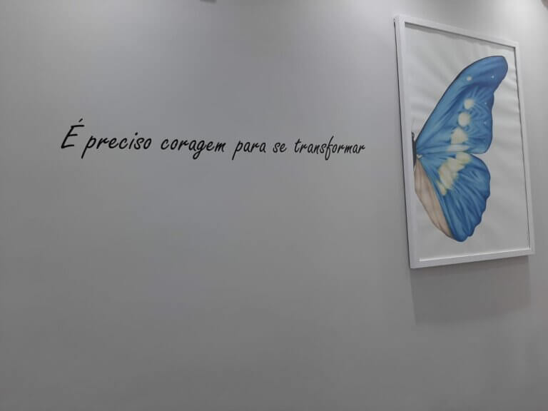 Parede com a frase "É preciso coragem para se transformar" e quadro de borboleta
